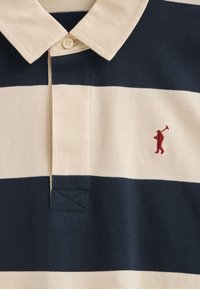 Koszulka polo w granatowo-kremowe poziome paski, z kołnierzykiem, z małą czerwoną haftowaną postacią trzymającą kij golfowy.