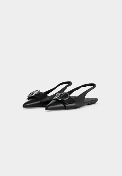 Μαύρα δερμάτινα μποτάκια slingback με μυτερά δάχτυλα και μεγάλες κυκλικές ασημένιες αγκράφες στους μπροστινούς ιμάντες, εμφανισμένα σε απλό φωτεινό φόντο.