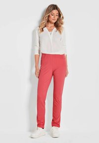 Rote Hosen mit hoher Taille und Seitentaschen, kombiniert mit einem weißen Langarmoberteil mit V-Ausschnitt und entspanntem Schnitt.