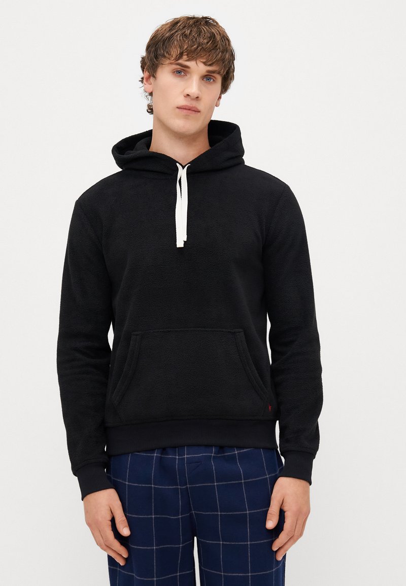 Μαύρη φλις μπλούζα με τσέπη καγκουρό, λευκές κορδόνες, ριμπ μανσέτες και στρίφωμα; φορεμένη με καρό πιτζάμα. Μαλακή υφή.