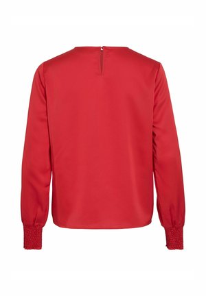 Top rosso a maniche lunghe con colletto alto, chiusura a chiave sul retro e polsini smock, caratterizzato da una texture liscia e un colore solido.