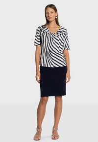 Granatowo-biały top w paski z dekoltem z drapowaniem, krótkimi rękawami oraz dopasowaną granatową spódnicą. Modelka ma na sobie srebrne sandały na paski.