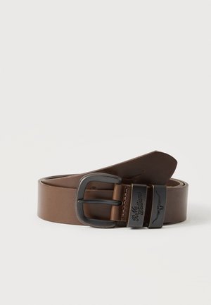 Ceinture en cuir marron avec boucle en métal foncé et deux passants, un passant gravé de « R.M. Williams » et un logo longhorn.