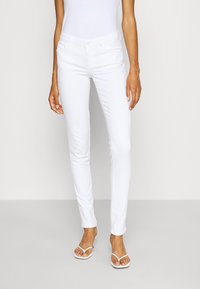 Slim-fit witte jeans van een katoenmengsel, met een klassiek ontwerp met vijf zakken en minimale hardware. Gecombineerd met witte slippers.