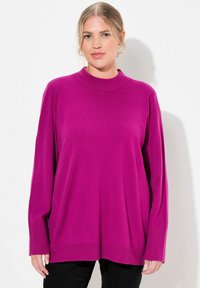 Fuchsiový oversized pulóver s vysokým golierom, dlhými rukávmi a rebrovanými manžetami. Mäkka textúra, minimalistický dizajn a bočné rozparky.