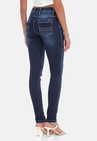 Skinny jeans in donkerblauwe denim met een gladde textuur, vijfzakkenontwerp en contrasterende stiksels. Gecombineerd met witte sandalen met hoge hakken.