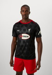 Jersey negra de manga corta con un patrón de diamantes, acentos rojos, logo del club y gráfico del patrocinador. Emparejada con pantalones cortos de un rojo brillante.