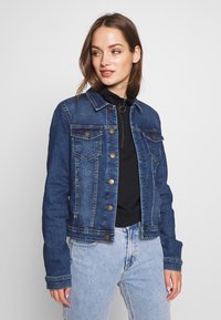 Dark blue denim jacket with a classic cut, button closure, two chest pockets, and a slightly faded texture. Worn over a black top.