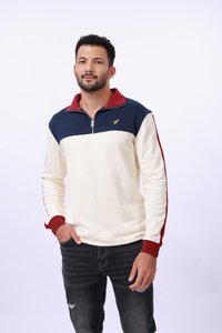 Sweatshirt crème zippé avec des accents bleu marine et bordeaux ; présente un petit logo doré sur la poitrine et des poignets côtelés. Porté avec un jean foncé.
