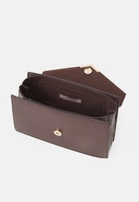 Brun läderplånbok med en slät yta, utrustad med en guldfärgad rund tryckknappslåsning och en inre fack för kort, med präglad varumärkesetikett synlig.