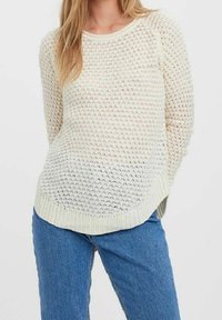 Pull en maille de couleur claire avec un motif de mailles ouvertes, un col rond et un ourlet côtelé. Associé à un jean bleu.