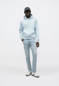 Lys blå hettegenser med kengurulomme, kombinert med lyseblå jeans og joggesko med grå detaljer. En grå caps fullfører antrekket.