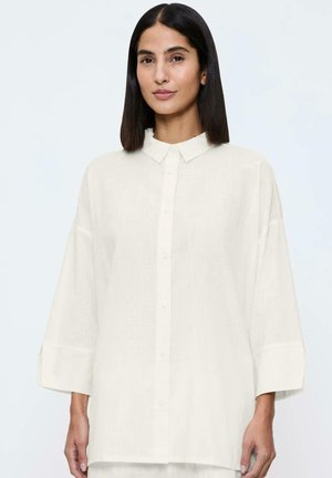 Biała lniana koszula z guzikami, z kołnierzykiem, opadającymi ramionami i długimi rękawami. Materiał ma teksturowany wygląd, zapewniający luźny krój.