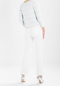 Vita vida jeans med utsvängd byxa, parat med en strukturerad ljusblå jacka med geometriskt mönster. Modellen bär silverfärgade högklackade skor.