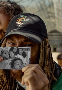 Czarna czapka z kolorowym haftowanym wzorem, noszona przez osobę trzymającą czarno-białe zdjęcie uśmiechających się dzieci. Widoczne tekstura i szczegóły.