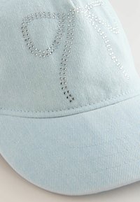 Hellblauer Denim-Cap mit einer strukturierten Oberfläche und Strassakzenten in einem fließenden Muster an der Vorderseite. Design mit gebogener Krempe.