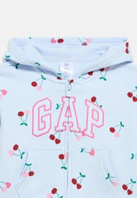 Γαλάζιο φούτερ με φερμουάρ και σχέδιο κερασιών, με ροζ κεντημένο λογότυπο "GAP" και τσέπες στο μπροστινό μέρος. Μαλακό ύφασμα, casual σχεδιασμός.