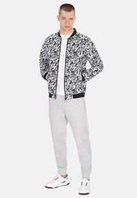 Svart och vit bomberjacka med ett grafiskt mönster, i kombination med gråa sweatpants och vita sneakers. Enligt design med ribbad mudd.