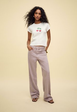 White short-sleeve t-shirt featuring red cherry print, paired with light pink wide-leg trousers. The background is a soft beige.