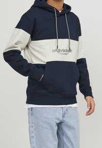 Hoodie color bloc marine et crème avec cordon de serrage, poche frontale et logo brodé. Fabriqué en tissu doux avec une coupe décontractée.