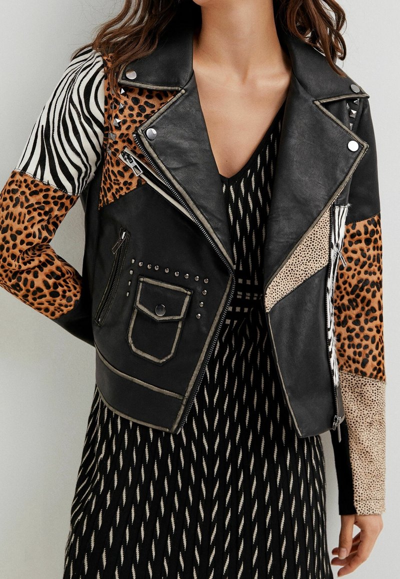 Giubbotto di pelle nera da biker con pannelli in stampa animale, borchie argentate e maniche a contrasto in motivi zebra e leopardo.