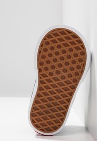 Podeszwa gumowego buta sportowego z teksturowanym, plastra miodu wzorem w brązowym kolorze, otoczona białą gumą. Podeszwa ustawiona na jasnym tle.