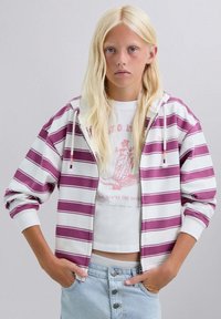 Sudadera con capucha con cremallera, con rayas púrpuras y blancas y cordón ajustable. Tela suave, corte relajado, puños acanalados, llevada sobre una camiseta gráfica blanca y pantalones cortos de mezclilla.