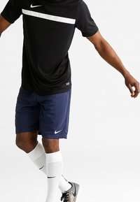 Nike black athletic t-shirt with a white horizontal stripe and logo, paired with navy shorts, white socks, and black sneakers.