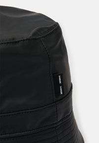 Chapéu de balde preto feito de material suave, com detalhes costurados e um rótulo destacando "Samsøe Samsøe" de um lado.