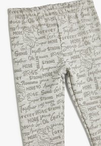 Grå leggings med en blanding af glitrende tekst og et unicorn-design, med en elastisk talje og en tætsiddende pasform. Forskellige positive ord er spredt ud over det hele.