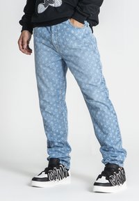 Jeans de mezclilla azul claro con un patrón repetido de logos, corte recto y bolsillos laterales, combinados con zapatillas altas negras.