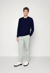 Camisola azul-marinho, calças cinza-claro e sapatos brancos. A camisola tem punhos canelados, as calças são afuniladas e os sapatos têm sola grossa.