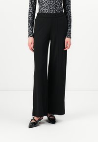 Black wide-leg pants made of a smooth fabric, featuring a stretchy waistband. Paired with a fitted, leopard-print long-sleeve top and pointed shoes.