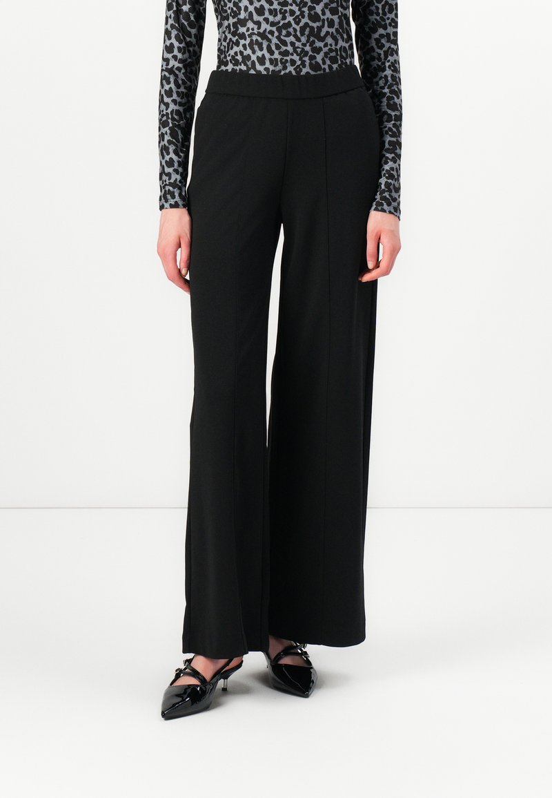 Black wide-leg pants made of a smooth fabric, featuring a stretchy waistband. Paired with a fitted, leopard-print long-sleeve top and pointed shoes.