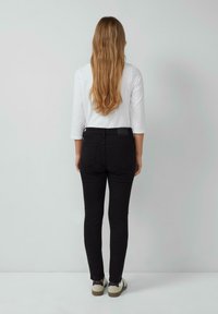Zwarte skinny jeans met een middelhoge taille, achterzakken en een soepele textuur, gecombineerd met een witte blouse met lange mouwen en casual schoenen.