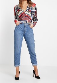 Langærmet mønstret skjorte med røde, blå og guld accenter, parret med opfrankede blå jeans og sorte stiletter.