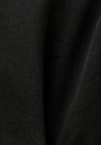 Gros plan d'un tissu noir montrant une fine texture de tissage diagonal et des plis doux.