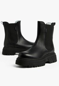 Zwarte leren enkellaarzen met elastische zijkanten, een chunky rubberen zool en een gladde textuur met een aantrekloopje aan de achterkant.