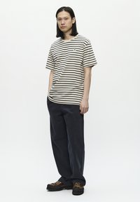 Tricou din bumbac rayé bej și negru, cu o croială lejeră. Asortat cu pantaloni largi de o nuanță închisă de bleumarin și pantofi caproi, rezistenți, cu șireturi.