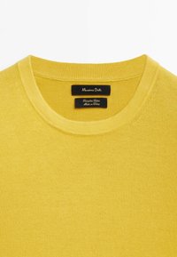 Yellow cotton crew neck sweater, featuring a smooth texture and subtle stitching details. Labels are black with white text, indicating brand and care.