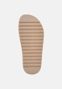 Sole di scarpa beige chiaro con scanalature orizzontali e punta arrotondata. Presenta il logo "GUESS" stampato sulla superficie. Texture liscia in tutta la superficie.