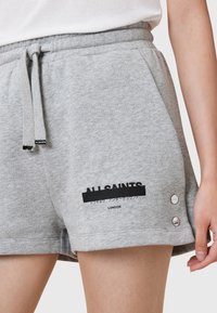 Shorts en coton gris avec une taille élastique, présentant un cordon de serrage et des boutons latéraux. "ALL SAINTS LONDON" imprimé en noir. Texture douce.