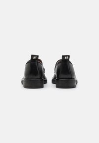 Black leather shoes featuring a sleek design, square heel, and distinctive metal accents on the back for style and detail.