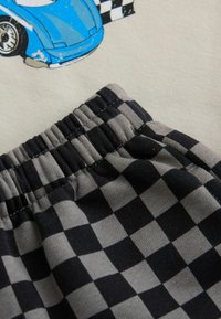 Cintura elástica con tela de cuadros negros y grises debajo de una impresión azul de coche sobre tela de ropa de color claro.