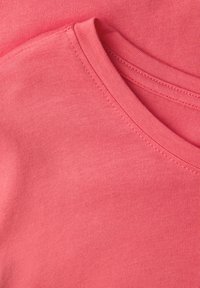 Bawełniany t-shirt z okrągłym dekoltem, miękką fakturą i intensywnym koralowym kolorem z widocznymi detalami przeszyć.