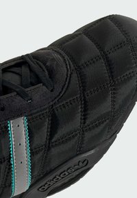 Čierne textilné topánky s vystuženým prešívaným zvrškom, zdobené akcentmi v odtieni teal a striebristými prvkami, s gumovou podrážkou a vyrazeným logom.