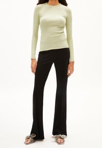 Jasnozielona, prążkowana bluzka z długim rękawem w połączeniu z czarnymi spódnicami dzwonami i szarymi sandałami z kokardą. Materiał wydaje się miękki i ma dopasowany fason.