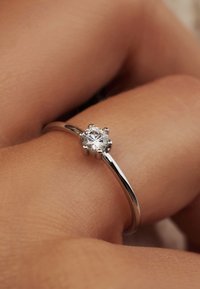 Bague en argent avec un superbe diamant rond en son centre, monté sur six griffes, accompagnée d'un anneau lisse et poli. Teint de peau en arrière-plan.