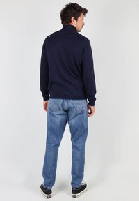 Un pull marin à col montant, associé à un jean bleu clair. La tenue présente une texture subtile et une coupe décontractée.