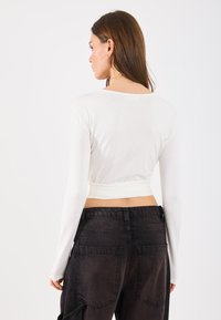 Top corto bianco a maniche lunghe con scollo rotondo, abbinato a jeans neri a vita alta con grandi tasche e una texture leggermente sbiadita.